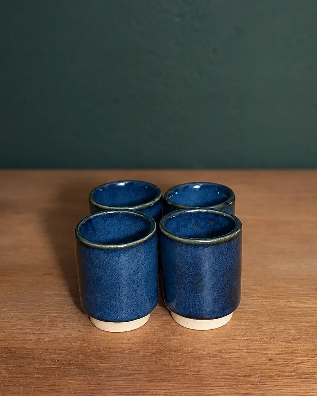 Kit com 4 copinhos, em cerâmica feita à mão por Pauliria Queiroz, sobre a prateleira do ateliê