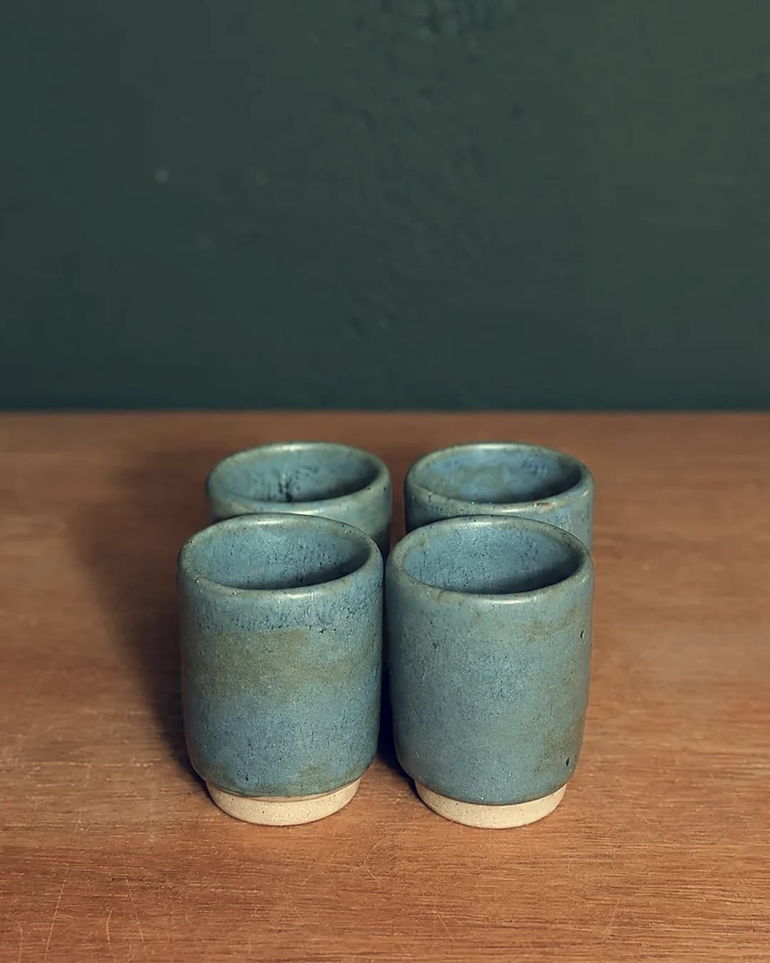 Kit com 4 copinhos, em cerâmica feita à mão por Pauliria Queiroz, sobre a prateleira do ateliê