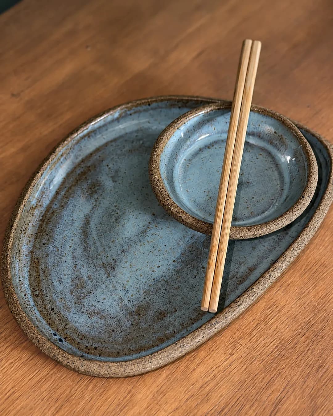 Kit sushi (prato e molheira), em cerâmica feita à mão por Pauliria Queiroz, sobre a prateleira do ateliê