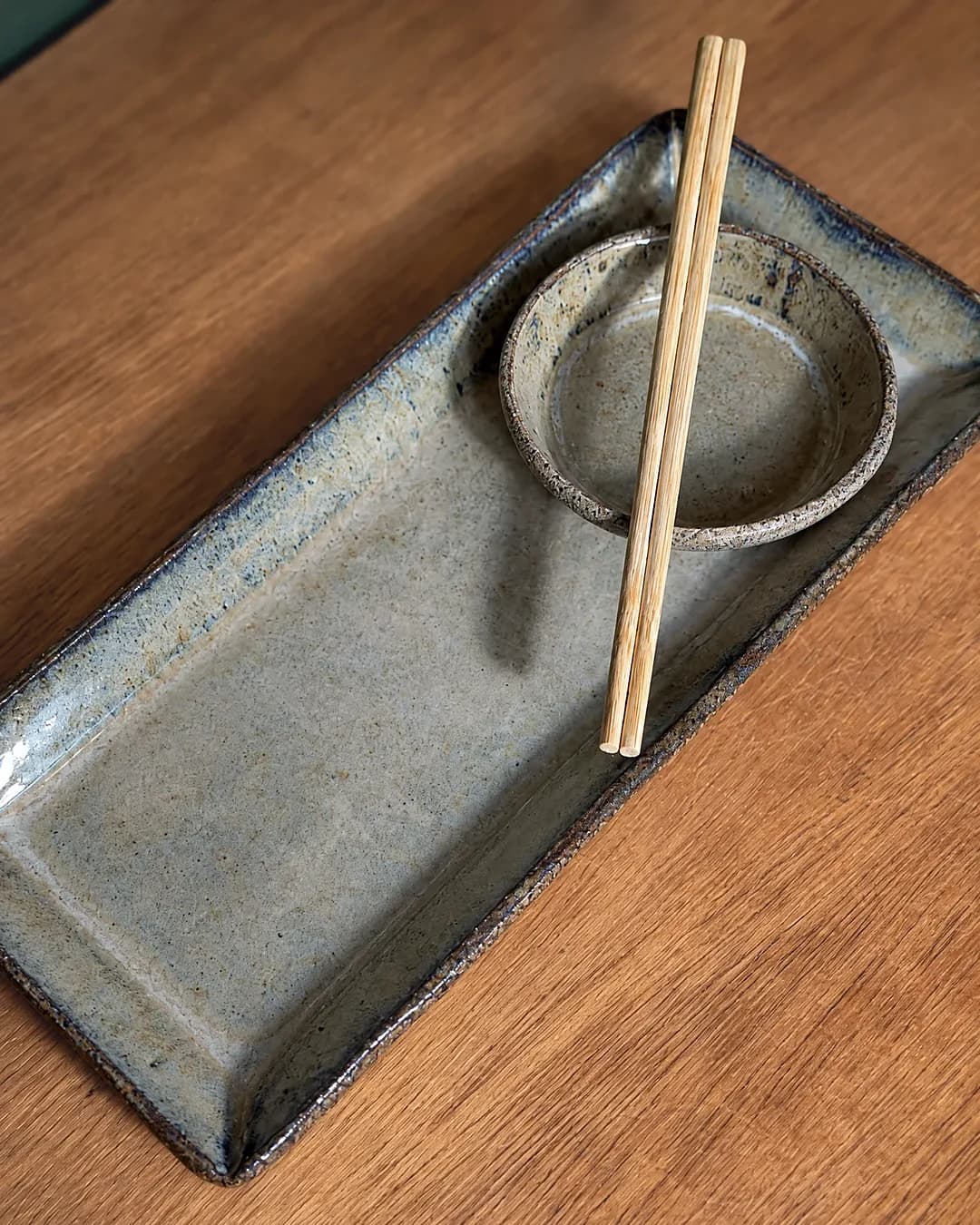 Kit sushi (prato e molheira), em cerâmica feita à mão por Pauliria Queiroz, sobre a prateleira do ateliê