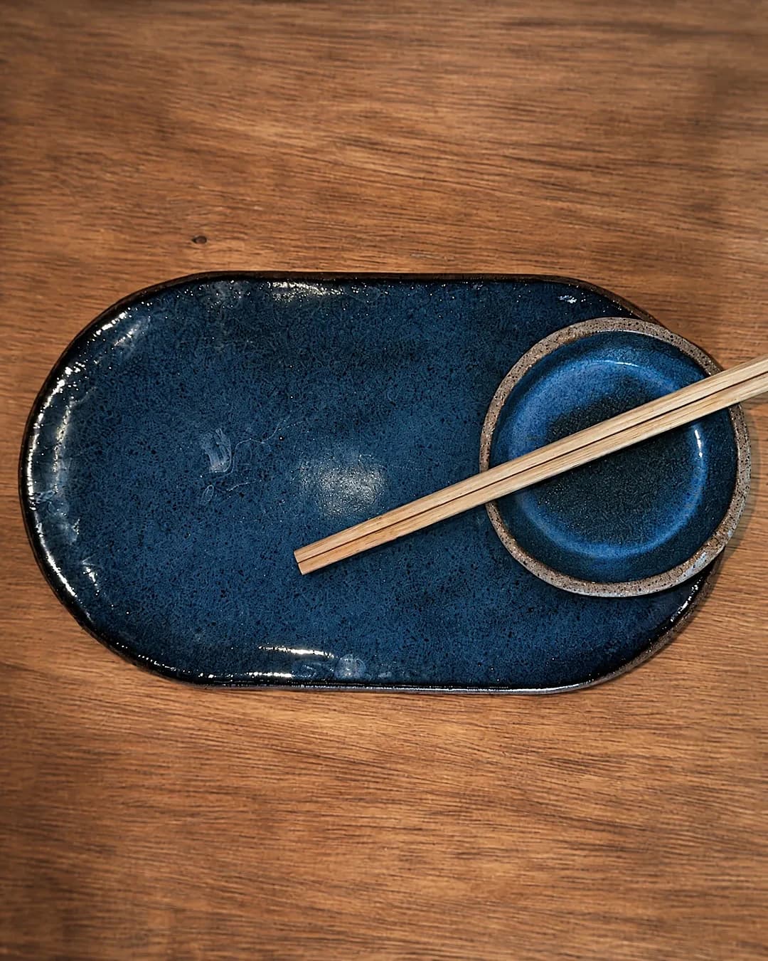 Kit sushi (prato e molheira), em cerâmica feita à mão por Pauliria Queiroz, sobre a prateleira do ateliê
